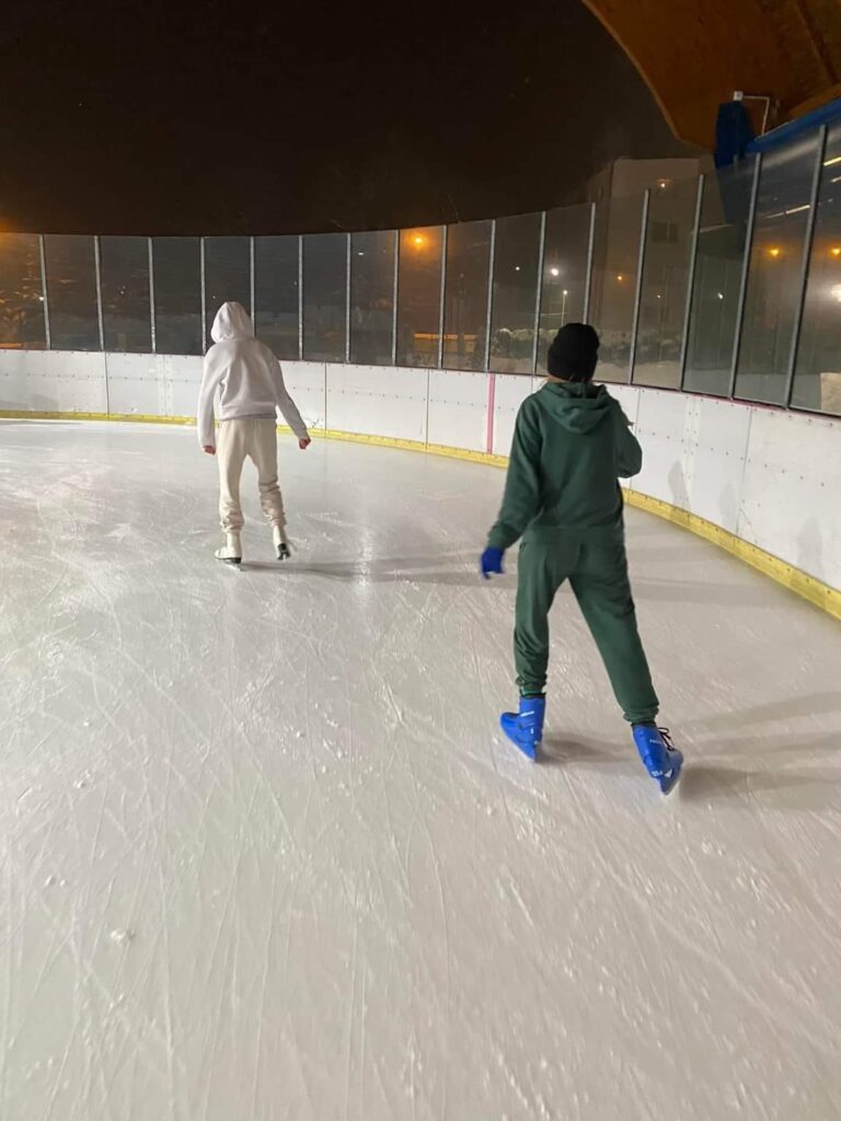 Dwoje dzieci jeździ na łyżwach na lodowisku.