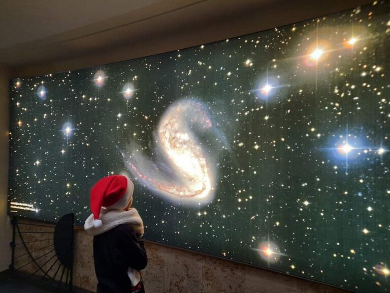 Chłopiec w czapce mikołaja podziwia duży plakat z planetami.