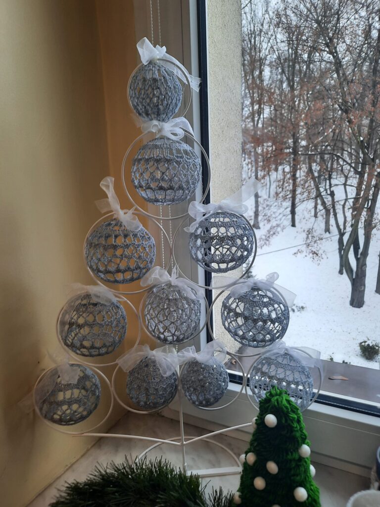 Zdjęcie przedstawia choinkę na stelażu, która jest ozdoniona bombkami.